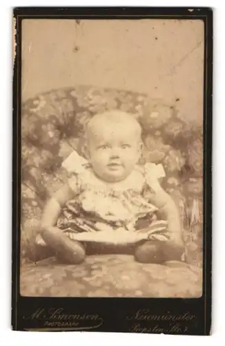 Fotografie M. Simonsen, Neumünster, Propsten Strasse 7, Lächelndes Baby auf einem Sitzmöbel