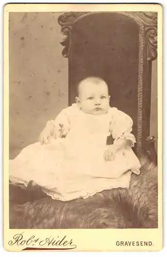 Fotografie Robt. Hider, Gravesend, 183, Parrock Street, Süsses Kleinkind im Kleid sitzt auf Fell