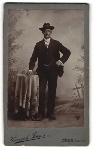Fotografie Heinrich Franze, Ybbs a. d. D., Herr mit Hut vor Studiokulisse