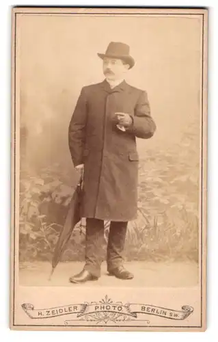 Fotografie H. Zeidler, Berlin, Jerusalemerstr. 59, Portrait stattlicher Herr mit Hut und Schirm im Mantel
