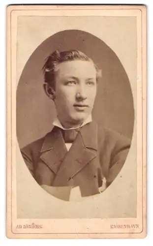 Fotografie Ad. Lönborg, Kjöbenhavn, Gl. Amagertorv 6, Junger Mann mit verwehter Frisur im grauen Anzug