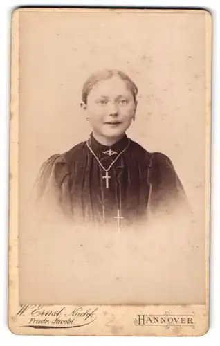 Fotografie W. Ernst Nachf., Hannover, Angerstr. 13 a, Lächelndes junges Mädchen mit Samtrobe und Kreuz um den Hals