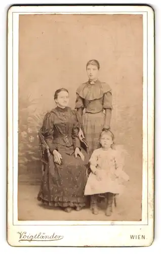 Fotografie Voigtänder, Wien, Mutter mit ihren beiden Töchtern in schicken Kleidern im Atelier, Mutterglück