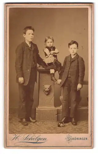 Fotografie H. Schilgen, Schöningen, Gruppe von 2 Jungen und einem Mädchen vor Säule mit Löwenkopf