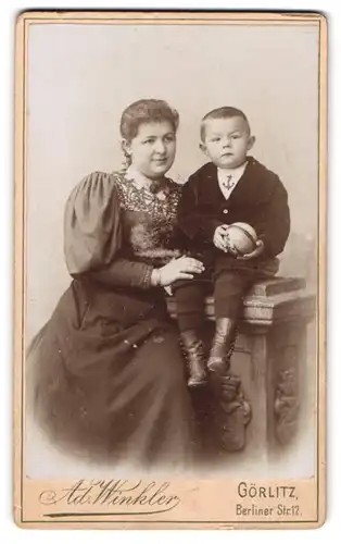 Fotografie Ad. Winkler, Görlitz, Mutter im Kleid mit Puffärmeln neben Söhnchen auf Konsole sitzend, Mutterglück
