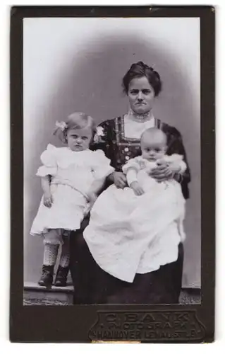 Fotografie C. Bank, Hannover, Mutter mit ihren zwei Kleinkindern, Tochter mit Zöpfen und Schleifen im Haar, Mutterglück