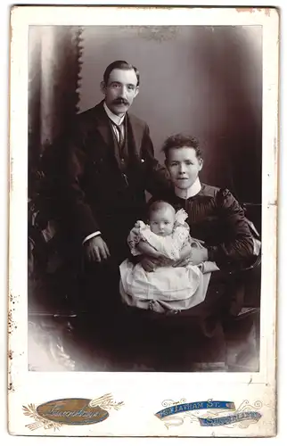 Fotografie Humphreys, Sunderland, Mutter und Vater mit Kleinkind im Kleidchen auf dem Schoss, Mutterglück