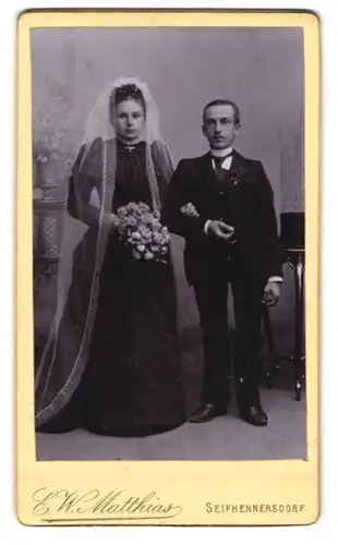 Fotografie E. W. Matthias, Seifhennersdorf, Brautpaar im schwarzen Kleid mit Puffärmeln und Mann im Anzug