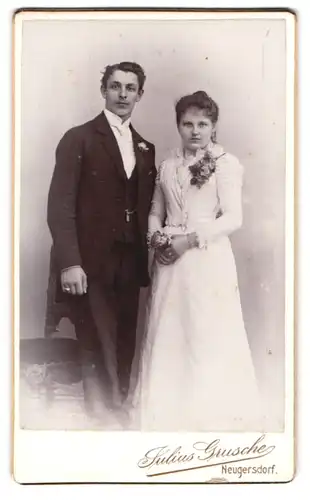 Fotografie Juluis Grusche, Neugersdorf i. S., Junges Brautpaar im weissen Kleid und Anzug mit Blumenbrosche