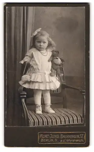 Fotografie Kurt Jung, Berlin, kleines Mädchen im weissen Kleid mit Teddybär im Arm, Haarschleife