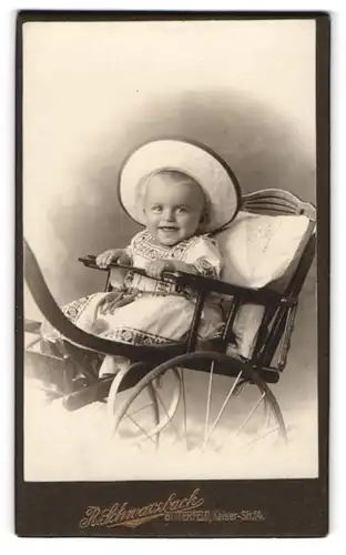 Fotografie R. Schwarzbach, Bitterfeld, Kleinkind im Kleidchen sitzt im Kinderwagen mit Hut