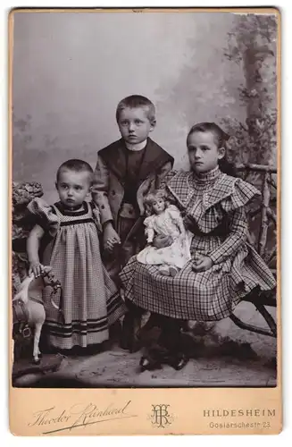 Fotografie Theodor Reinhard, Hildesheim, drei Kinder in Kleidern und Anzug mit Puppe und Spielzeug Pferd