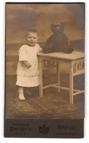 Fotografie Otto Witte, Berlin, Kleinkind im Kleidchen mit grossen Teddybär auf dem Tisch, 1916