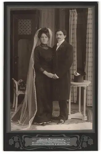 Fotografie Julius Grunewald, Oberneukirch, Braut im schwarzen Kleid mit Schleier neben ihrem Mann im Anzug