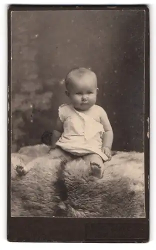 Fotografie unbekannter Fotograf und Ort, Süsses Kleinkind sitzt auf einem Fell
