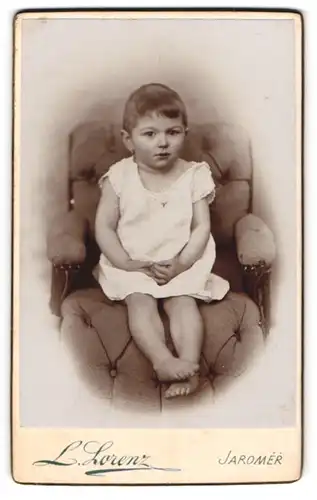 Fotografie L. Lorenz, Jaromer, entzückendes Kind in weissem Kleid auf einem elegaten Sessel