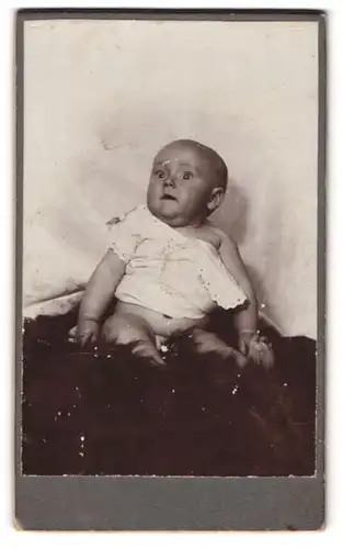 Fotografie unbekannter Fotograf und Ort, Entzückendes Kleinkind in weissem Oberteil auf Pelz