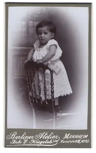 Fotografie E. Kregeloh, Mannheim, Kunststrasse 12, Niedliches Kleinkind in weissem Kleidchen auf einem Stuhl
