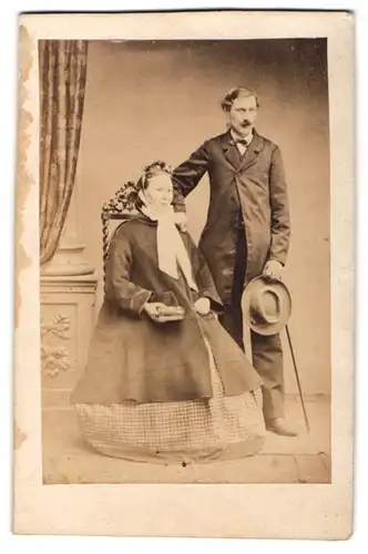 Fotografie unbekannter Fotograf und Ort, Portrait Paar im karierten Reifrockkleid mit Mantel und Herr im Anzug