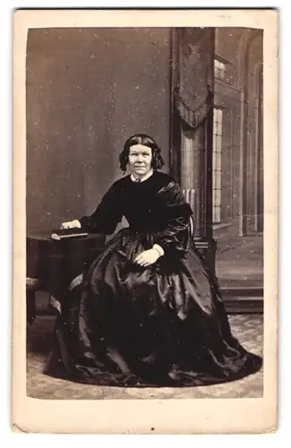 Fotografie A. H. Calrke, Ripon, ältere Dame im schwarzen Seidenkleid mit Korkenzieherlocken