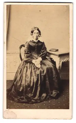 Fotografie J. & T. Spencer, Leicester, junge englische Dame in seidenen Kleid mit Haube posiert im Atelier