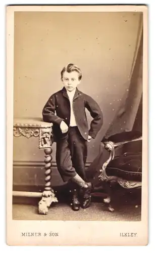 Fotografie Milner & Son, Ilkley, junger Knabe im Anzug mit halb langen Hosen steht posierend im Atelier