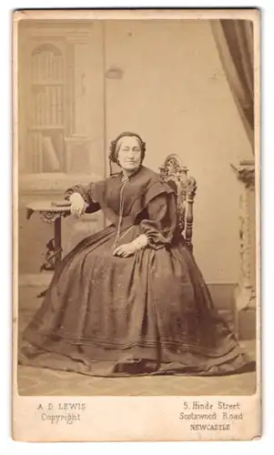 Fotografie A. D. Lewis, Newcastle, ältere Dame im schlichten Biedermeierkleid mit Haube sitzend am Tisch