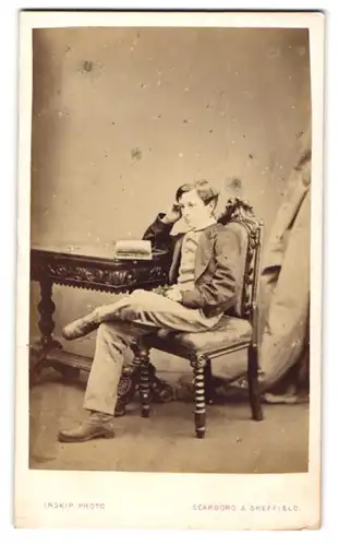Fotografie Inskip, Scarboro, junger Knabe im Anzug sitzend am Tisch mit aufgeschlagenem Buch