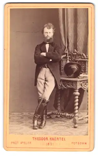 Fotografie Theodor Haertel, Potsdam, Herr im Anzug mit Lackstiefeln und Zylinder auf dem Tisch, Vollbart