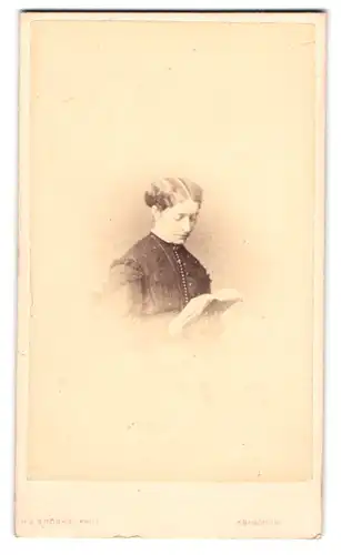 Fotografie Henry J. Brooks, Abingdon-on-Thames, junge Frau im dunklen Kleid sitzt lesend im Atelier