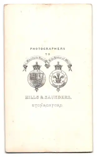 Fotografie Hills & Saunders, Eton, junger Engländer im Anzug sitzt breitbeinig im Atelier