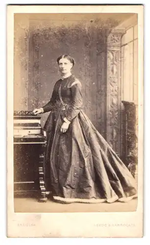 Fotografie Skeolan, Leeds, Porträt Dame im Biedermeierkleid posiert stehend am Sekretär