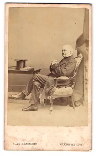 Fotografie Hills & Saunders, Oxford, älterer englischer Herr im Anzug mit Zylinder auf dem Tisch
