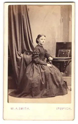 Fotografie W. A. Smith, Ipswich, junges englisches Mädchen im dunklen Reifrockkleid sitzend am Tisch