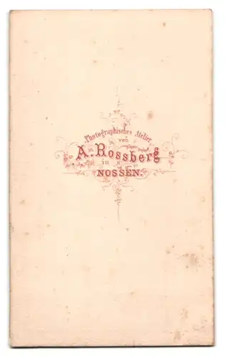 Fotografie A. Rossberg, Nossen, junger Mann im langen Mantel posiert stehend am Sekretär