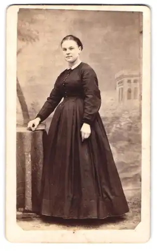 Fotografie unbekannter Fotograf und Ort, Portrait junge Frau im schwarzen Kleid posiert vor einer Studiokulisse