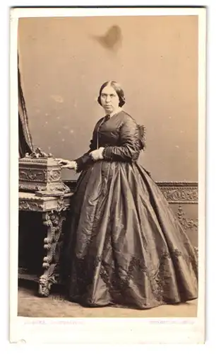 Fotografie Jno. Hawke, Devon, Dame im Biedermeierkleid mit Halskette posiert stehend am Sekretär