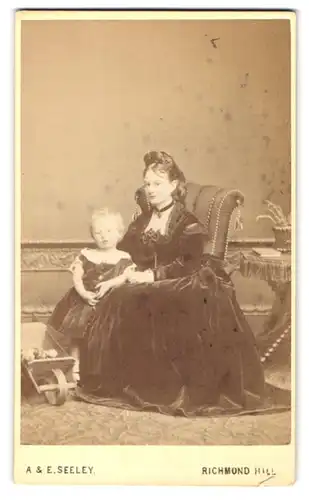 Fotografie A. & E. Seeley, London-Richmond Hill, junge Mutter im Samtkleid mit Töchterchen im schulterfreien Kleid