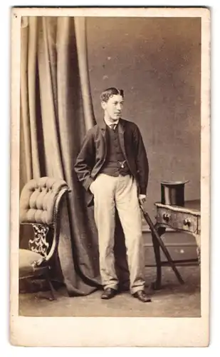 Fotografie Hills & Saunders, Eton, junger Mann im Anzug mit heller Hose und Schirm, Zylinder auf dem Tisch