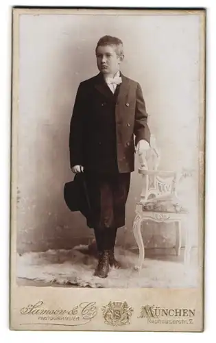 Fotografie Hanson & Co., München, Junge im schwarzen Anzug mit Knickerbockern zur Kommunion, 1903
