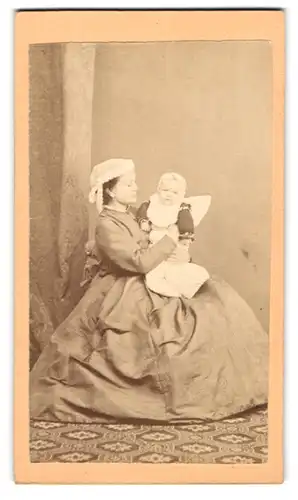 Fotografie unbekannter Fotograf und Ort, junge Mutter im Reifrockkleid mit ihrem Kind auf dem Schoss