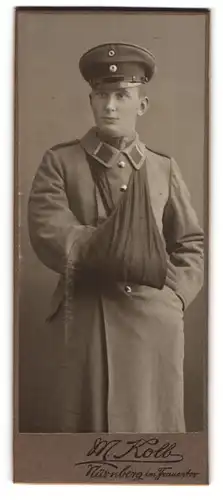 Fotografie M. Kolb, Nürnberg, im Frauentor, verwundeter Uffz. in Uniform Mantel mit Armschlinge