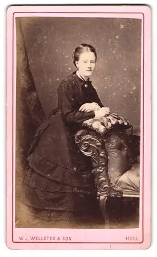 Fotografie W. J. Wellsted & Son, Hull, Paragon Street 19 & 20, gutbürgerliche Dame lehnt im eleganten Kleid am Sessel