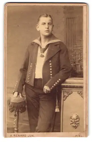 Fotografie A. Renard Jun., Kiel, Matros ein Uniform mit Matrosenknoten und Modell Segelschiff