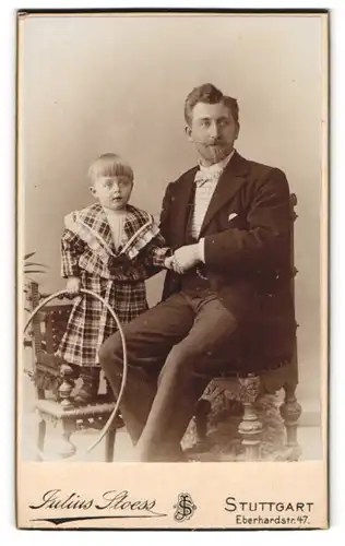 Fotografie Julius Stoess, Stuttgart, Vater im Anzug mit Tochter im karierten Kleid auf dem Stuhl, Vaterglück