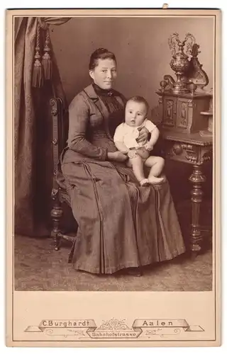 Fotografie C. Burghardt, Aalen, Mutter im gestreiften Kleid mit Kleinkind auf dem Schoss