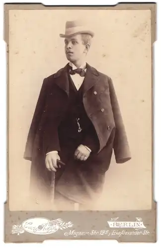Fotografie Georg Rogge, Berlin, junger blonder Mann im Anzug mit Mantel und Fliege trägt Hut