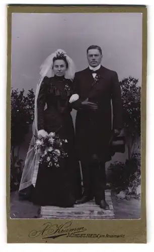 Fotografie A. Krumm, Mindelheim, Hochzeitspaar im schwarzen Kleid mit weissem Schleier und im Anzug mit Zylinder