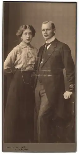 Fotografie Willy Wilcke, Hamburg, junges Paar im heller Bluse mit dunklem Rock und Herr im Anzug mit Krawatte