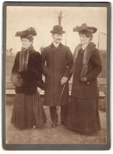 Fotografie unbekannter Fotograf und Ort, Herr mit zwei Damen in Pelzmänteln und im Anzug mit Melone und Flanierstock